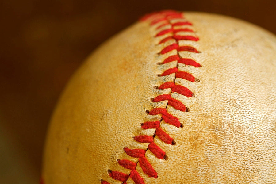 A modern bedroom with a workspace features the Baseball Three-quarter Wall Mural showcasing a close-up baseball. The room includes a computer desk, blue and yellow bed pillows, a soccer ball on the floor, and a white closet.