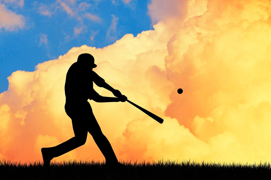 A bedroom showcases the vibrant Batter at Dusk Wall Mural, depicting a baseball player swinging against an orange cloud and blue sky. Sunlight fills the modern space, highlighting its bed, desk, computer, closet, and sleek décor.