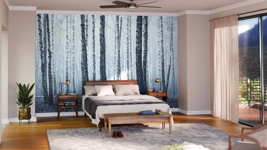 A modern bedroom features the Birch Trees Black and White Wall Mural behind the bed, with wooden furniture, plants, a plush rug, beige walls, and a large window with sheer curtains letting in natural light.