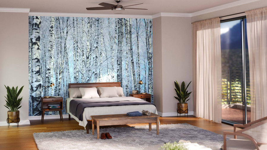 A modern open-plan living and dining room with wood floors, teal armchairs, a gray sofa, and a feature wall displaying the Birch Trees Pale Blue Sky Wall Mural. The dining area includes a dark wood table and pendant lights with kitchen views.