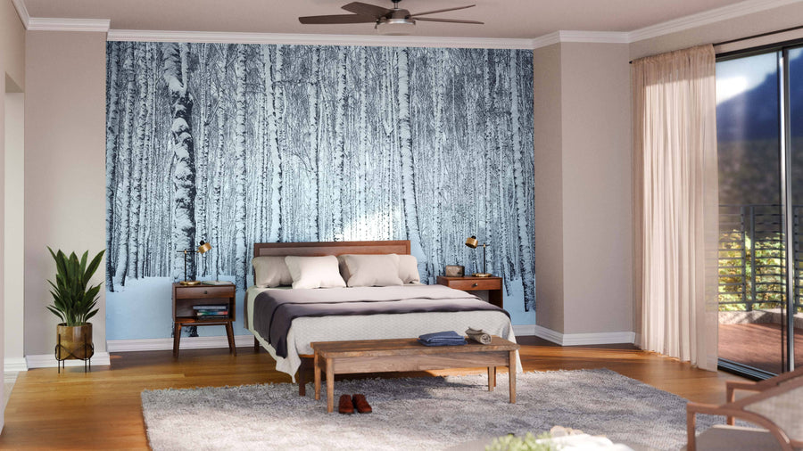 A cozy bedroom with a wooden bed, gray bedding, nightstands with lamps, a bench, and a large Black and White Birch Tree Forest Wall Mural. A plant by the bed and sunlight through sheer curtains create an inviting retreat.