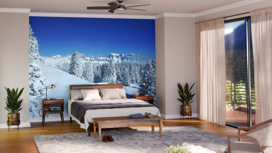 A modern living and dining room with wooden floors and mid-century furniture features the Blue Sky Winter in the Alps Wall Mural, showcasing snowy mountains and pine trees under a blue sky for added depth and a wintry vibe.