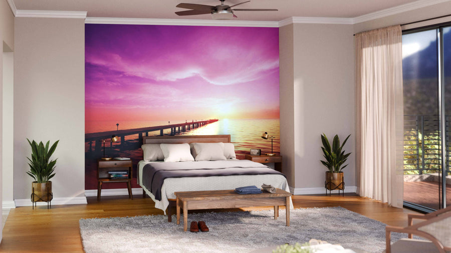 A modern open-plan living and dining room with wood floors, stylish furnishings, and a Boardwalk on Beach Wall Mural featuring a vibrant pink and orange sunset over a pier as a striking accent wall behind the living area.