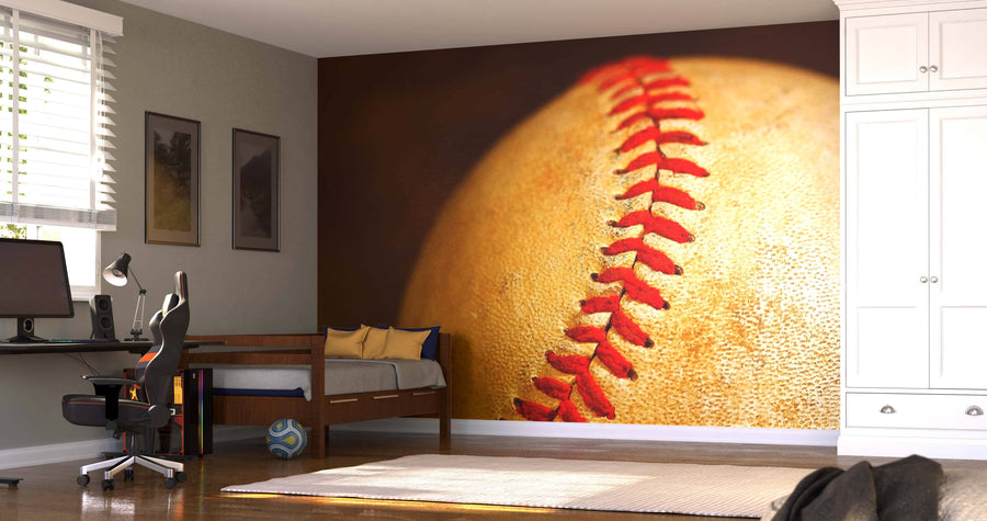 A modern bedroom with a workspace features the Baseball Three-quarter Wall Mural showcasing a close-up baseball. The room includes a computer desk, blue and yellow bed pillows, a soccer ball on the floor, and a white closet.