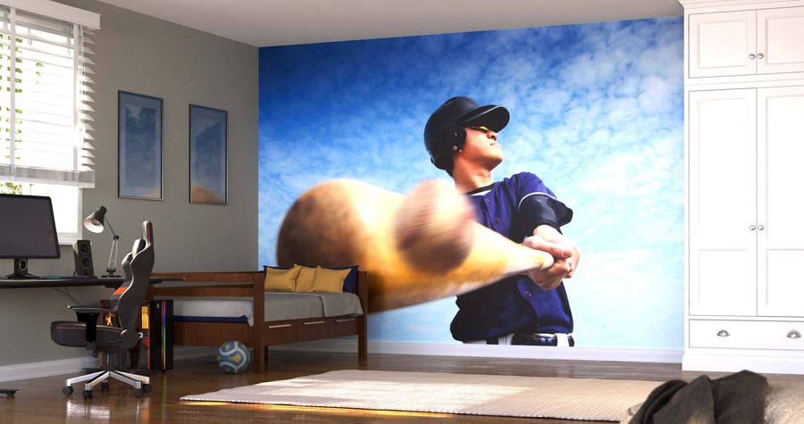 A modern bedroom showcases the Baseball Player Swinging Wall Mural against a blue sky, with a desk, daybed, framed art, soccer ball, white cabinets, carpeted floor, and sunlight streaming through the blinds.