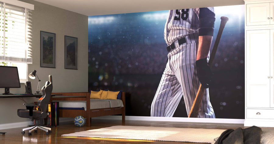 A modern bedroom with a desk, chair, and daybed features the Baseball Player Walking Wall Mural showing a pinstriped player with bat from the chest down. Natural light filters in through blinds, and a soccer ball sits on the floor.