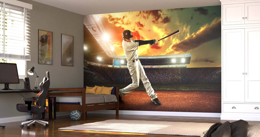 A bedroom features the Baseball Player in Action Wall Mural showing a batter in a stadium at sunset, along with a bed, computer desk, chair, shelves, soccer ball, closet, and sunlight streaming through left-side blinds.