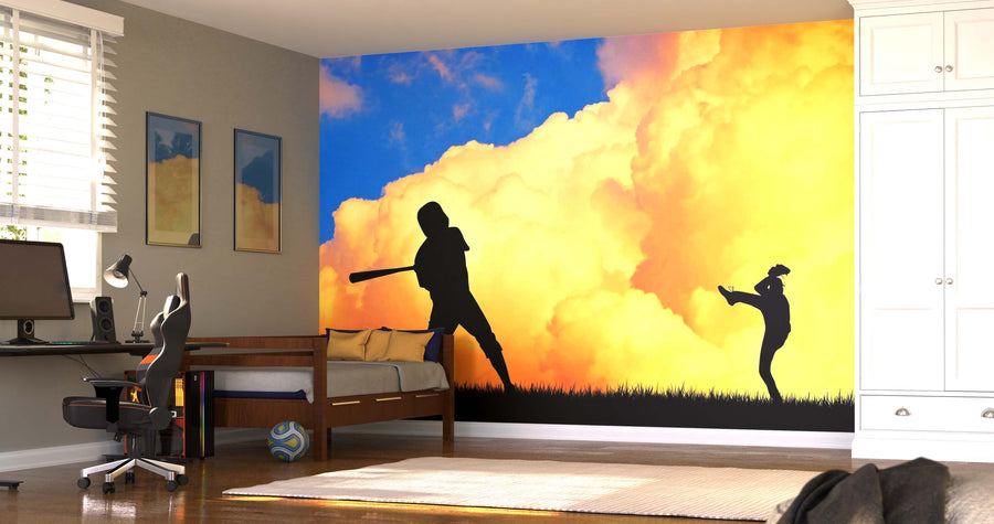 A bedroom with a workspace, bed, and the Baseball Silhouettes Wall Mural—durable peel and stick wallpaper showing two players (pitcher and batter) set against a bright orange-cloud sky. Sunlight streams through blinds; a ball lies near the bed.