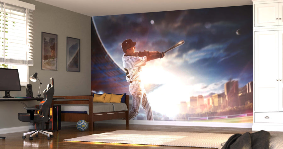 A sunlit bedroom with a computer desk, chair, and bed showcases the Big League Swing Wall Mural—featuring a baseball player swinging a bat in a stadium with bright lights. Wood floors, wall art, and white built-in cabinets complete the personalized space.