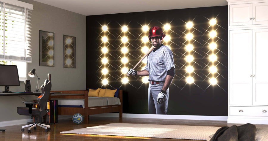 A modern bedroom with a desk and bed features the Game Face On Wall Mural, showing a baseball player holding a bat under bright lights. Sports-themed decor includes a soccer ball and natural light filling the space.