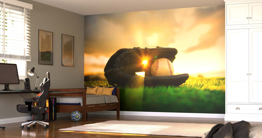 A sunlit bedroom features the Golden Hour Catch Wall Mural—a peel and stick mural of a baseball glove holding a ball against a bright sky. The room has a bed, computer desk, black chair, white cabinets, soccer ball, and framed art.