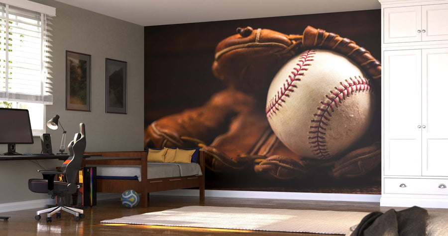 A bedroom with a desk, chair, and bed features the Leather Baseball Glove and Ball Wall Mural showing a close-up of a baseball in a glove. Sunlight streams in, and a blue and white soccer ball rests on the wooden floor by the bed.