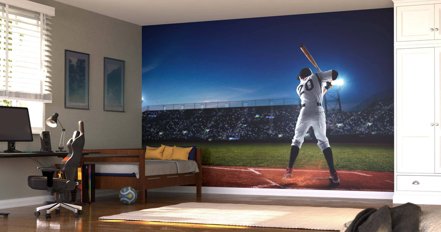 A bedroom features the Ready to Swing Wall Mural showing a baseball player at bat in a night stadium, plus a bed, desk, chair, sports decor, light wood floors, natural light, and a soccer ball near the bed.