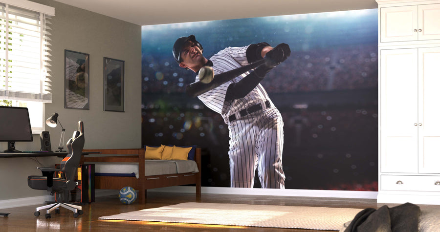 A bedroom showcases the Slugger in Action Wall Mural, depicting a baseball player swinging a bat in a stadium. The space includes a bed, desk with computer, chair, white cabinets, soccer ball on the floor, and sunlight streaming through blinds.