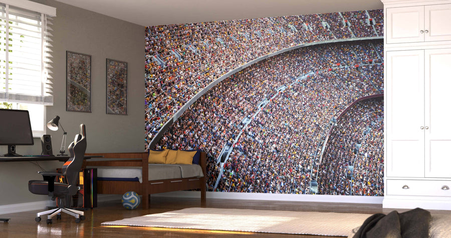 A modern bedroom features the Stadium Full of Fans Wall Mural, a desk with a computer, yellow pillows on the bed, a soccer ball beneath, framed pictures, large windows with blinds, wood floors, and a white wardrobe.