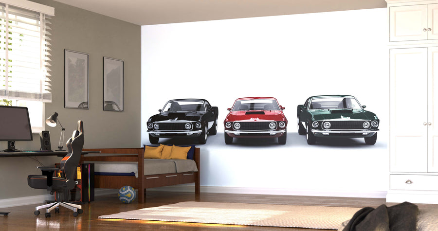 A modern bedroom with a desk, chair, bed, and wardrobe features the Vintage Muscle Cars Wall Mural showcasing three classic cars. Sunlight streams through white blinds on the window, brightening the space.
