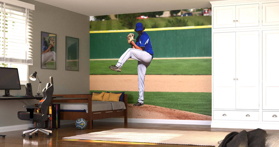 A bedroom with a desk and chair, single bed, soccer ball on the floor, white cabinets, and windows with blinds. The wall features the Winding Up Wall Mural showing a baseball pitcher in a blue uniform.