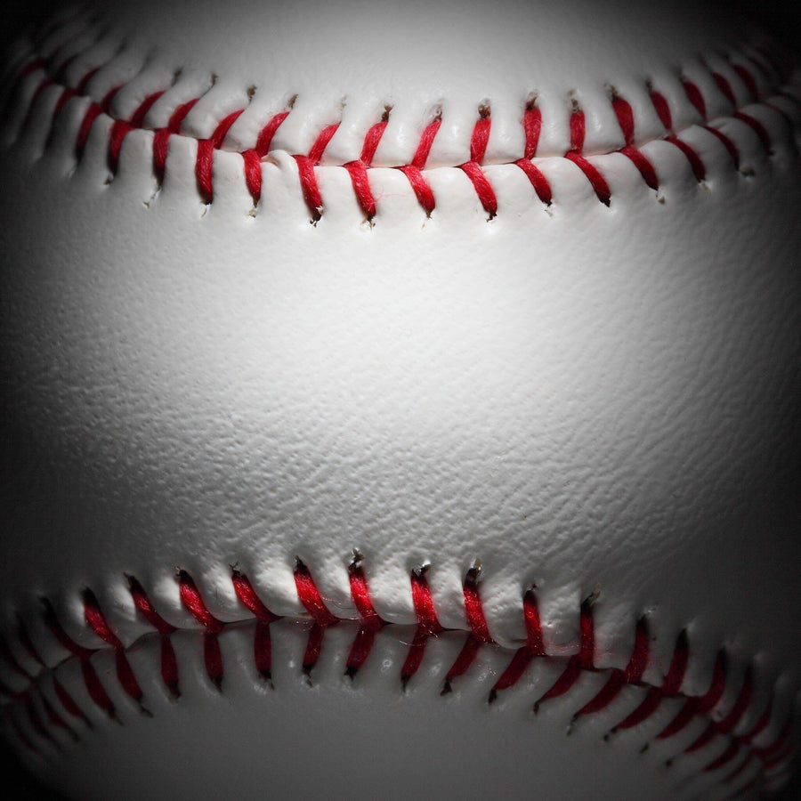 A bedroom features the Closeup of a Baseball Wall Mural, a modern desk with computer and chair, a daybed with yellow and gray pillows, wooden flooring, framed baseball art, a soccer ball, and white built-in wardrobes.