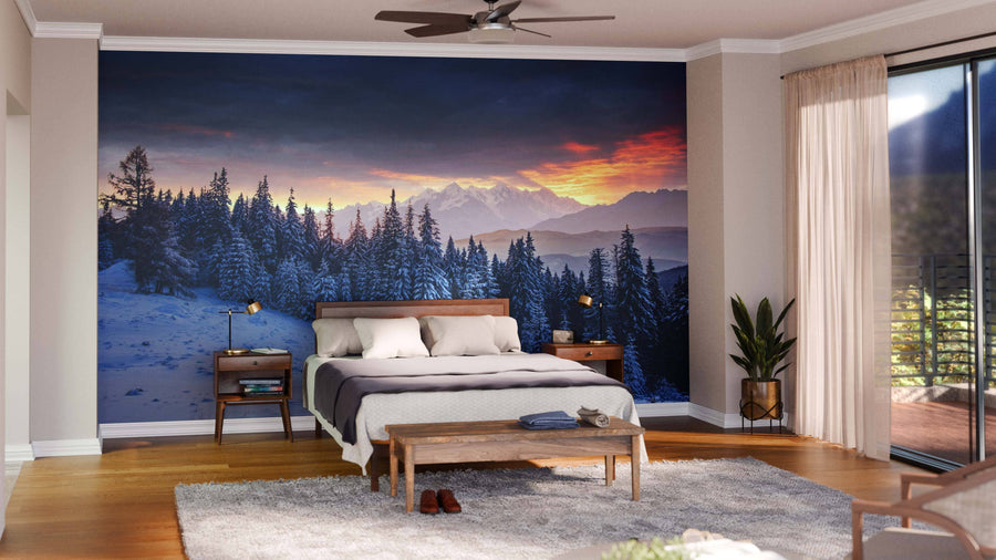 A modern living-dining room with wood floors features teal and wood furniture, a patterned rug, and the "Colorful Sunset Over the Mountain Wall Mural," creating a cozy atmosphere. Pendant lights hang above a dark dining table with six chairs.