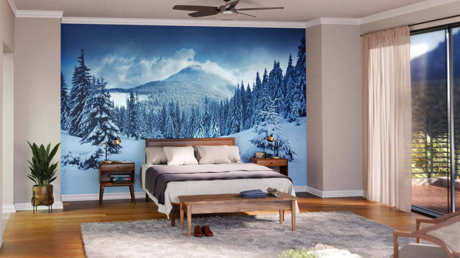 A modern living and dining room with wooden floors, teal armchairs, a large dining table, and the "Cottage in a Pine Tree Forest Wall Mural." Globe lights, plants, and rustic decor complete this stylish contemporary space.