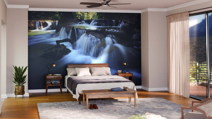 A modern living-dining room with wooden floors, teal chairs, a large dining table, and the Deep Forest of Thailand Wall Mural featuring a serene waterfall. The space is brightened by round pendant lights and accented with rugs and contemporary furniture.