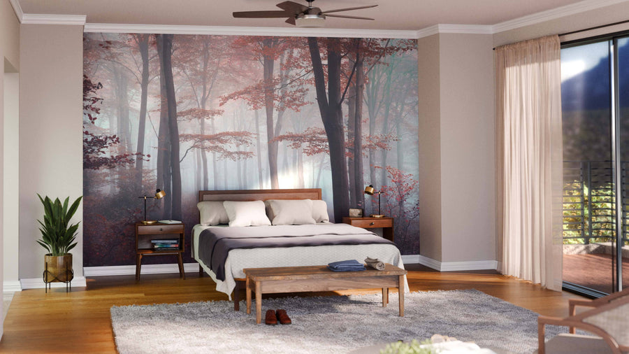 A cozy bedroom features the Fall Foggy Forest Wall Mural, depicting a misty forest with red-leaved trees. The room has a wooden bed, matching nightstands and lamps, a bench, gray rug, potted plant, sheer curtains, and a ceiling fan.