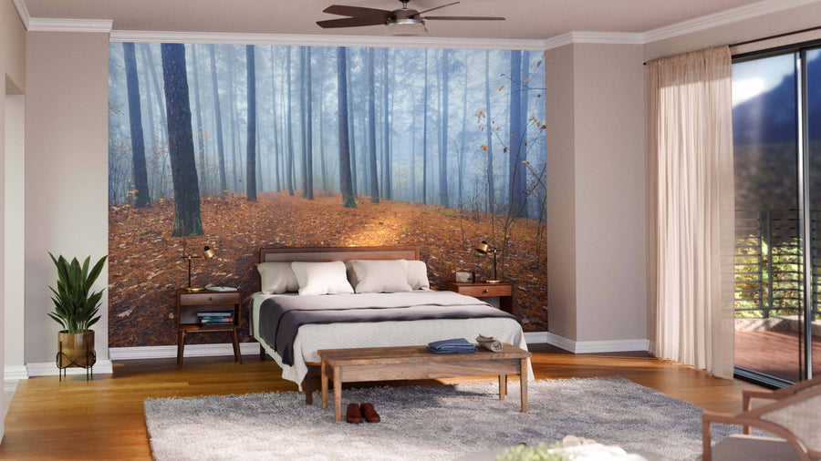 A cozy bedroom features the Foggy Autumn Forest Wall Mural behind the bed, with neutral walls, wood floors, white bedding with gray accents, potted plants, large windows, and sheer curtains creating a serene atmosphere.