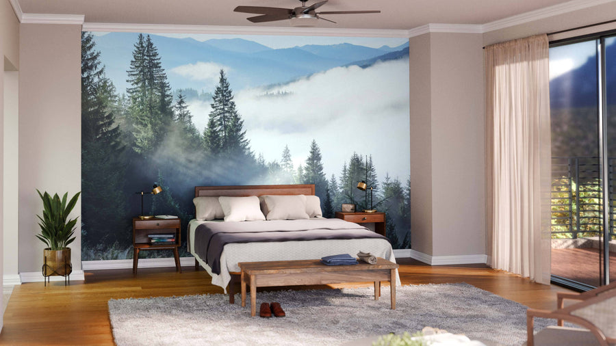 Modern bedroom with wood furniture, cozy bedding, and a glass door with beige curtains. The Foggy Forest in Mountains Wall Mural adds style above the bed, complemented by a bench, plant, lamps, rug, and wooden flooring.
