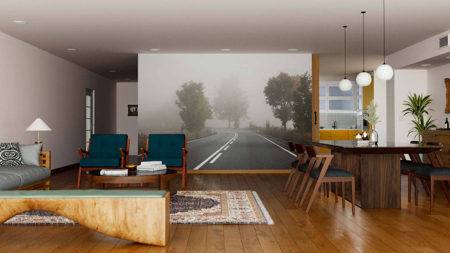 A modern living and dining area features wooden floors, a mix of upholstered and wood furniture, pendant lights over the table, cozy rugs, art accents, and a stunning Foggy Road Wall Mural depicting a misty road with trees.