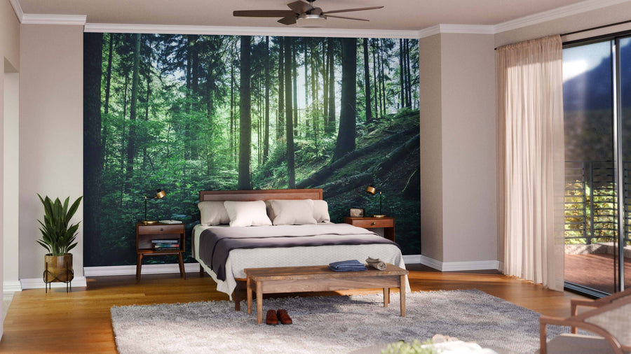 A modern bedroom showcases the Forest with Fallen Trees Wall Mural behind a wooden bed, with mid-century nightstands, neutral bedding, a bench, potted plant, gray rug, and sheer-curtained window creating a tranquil vibe.