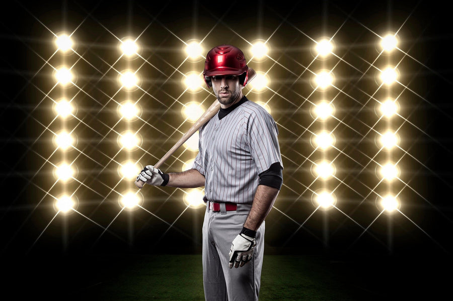 A modern bedroom with a desk and bed features the Game Face On Wall Mural, showing a baseball player holding a bat under bright lights. Sports-themed decor includes a soccer ball and natural light filling the space.