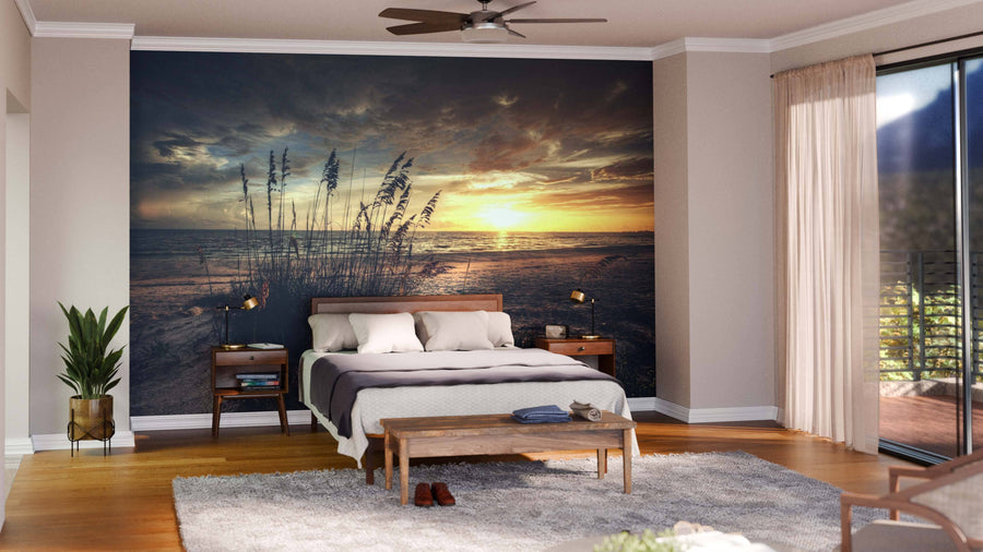 A modern living and dining room with wood flooring, mid-century furniture, globe pendant lights, and a Grassy Beach Sunset Wall Mural featuring clouds, tall grasses, and golden light reflecting on the water.