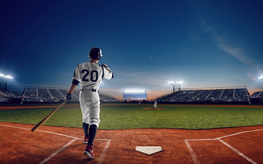 A bedroom with a desk, chair, and bed features the Home Run Wall Mural, showing a baseball player wearing number 20 at home plate in a brightly lit stadium at dusk. A soccer ball is on the floor near the bed.