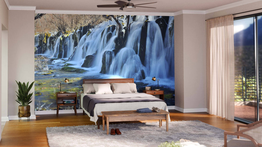 A modern living-dining room with wood floors and mid-century furniture features a Jiuzhaigou Valley Waterfalls Wall Mural as a nature-inspired focal point. Warm lighting and earth tones enhance the cozy atmosphere.