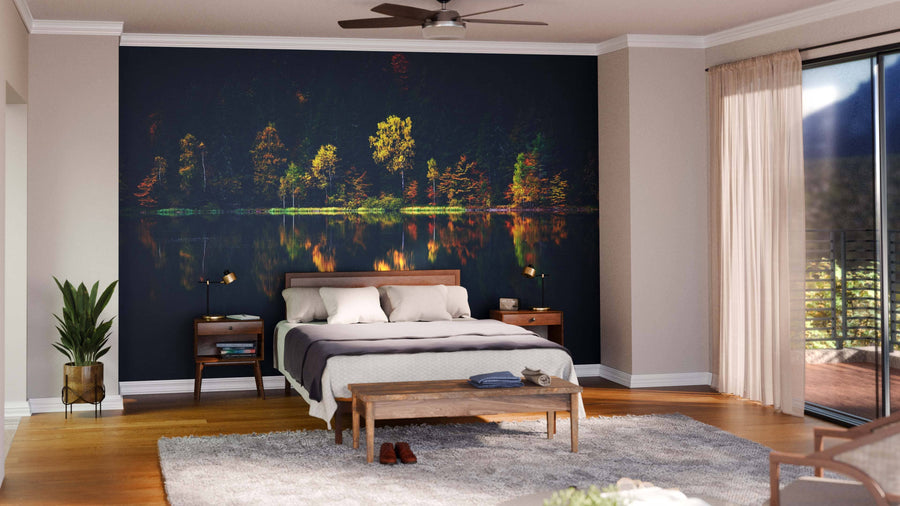 A modern open-concept living and dining room features wooden floors, mid-century furniture, pendant lights, a patterned rug, and the Lake Autumn Reflection Wall Mural—a peel and stick mural of illuminated trees reflected on water for a warm vibe.