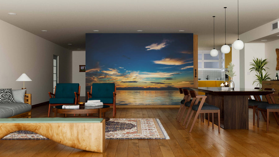 A modern open-plan living and dining room with wooden floors, teal armchairs, and the "Beautiful Sunset on Pacific Ocean Wall Mural." Cozy décor, rugs, and pendant lights create an inviting atmosphere.