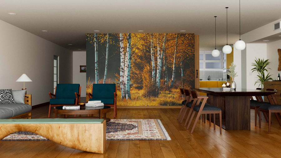 A modern living-dining room features wooden floors, teal and wood chairs, a gray sofa, a large dining table, and the Birch Trees In Autumn Forest Wall Mural dividing the space. Round pendant lights hang above the dining area.