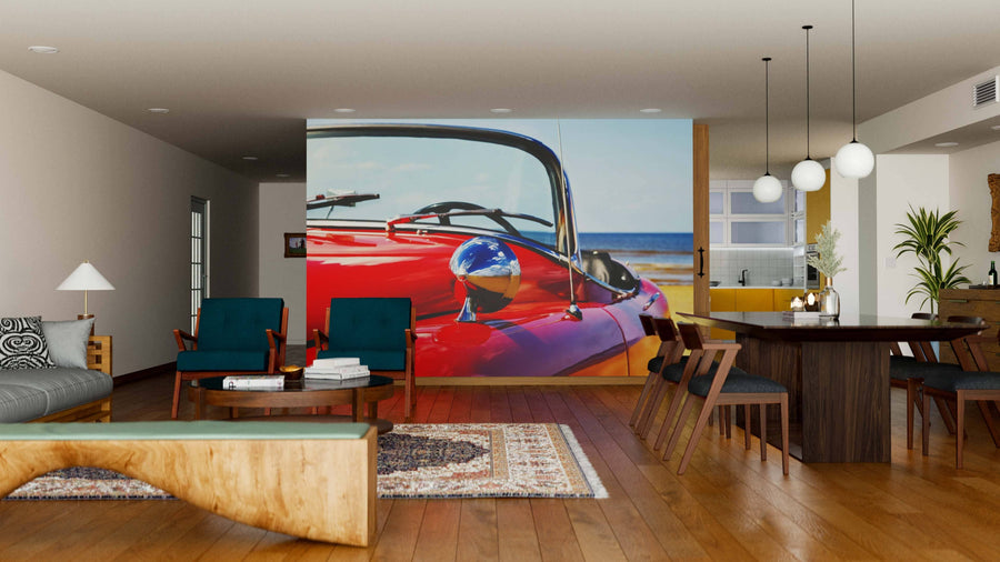 A modern open-plan living and dining area features wood floors, colorful chairs, a dining table, and a striking Classic Red Jaguar Wall Mural by the ocean—creating a vibrant retro focal point in this stylish space.