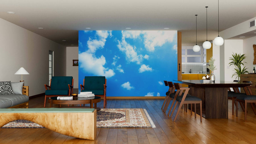 A modern living and dining room with wood floors, green chairs, a Clear Sky Wall Mural on the main wall, a dining table with globe lights, and a kitchen area in the background.