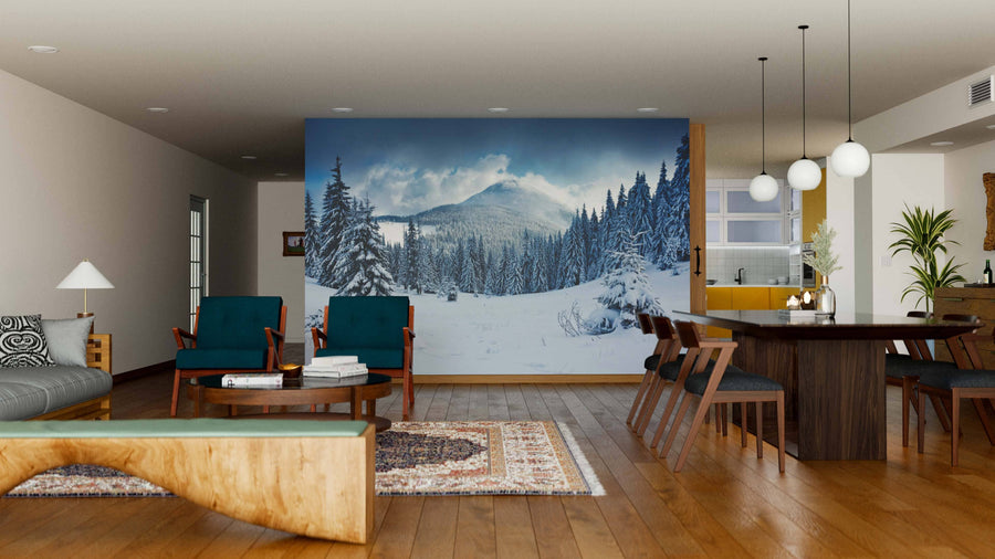 A modern living and dining room with wooden floors, teal armchairs, a large dining table, and the "Cottage in a Pine Tree Forest Wall Mural." Globe lights, plants, and rustic decor complete this stylish contemporary space.