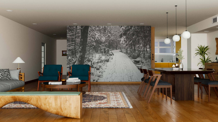 A modern open-plan living and dining room with wooden floors, teal armchairs, and a large Forest Landscape With Snow Wall Mural. The dining area has a dark table, wooden chairs, and globe pendant lights, with the kitchen visible in the background.