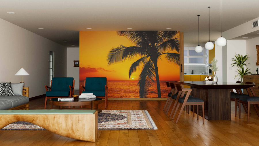 A modern living-dining area features wooden floors, teal chairs, and the Golden Tropical Sunset Wall Mural—a peel and stick mural of a palm tree sunset—plus a dark dining table, pendant lights, contemporary decor, and a cozy atmosphere.
