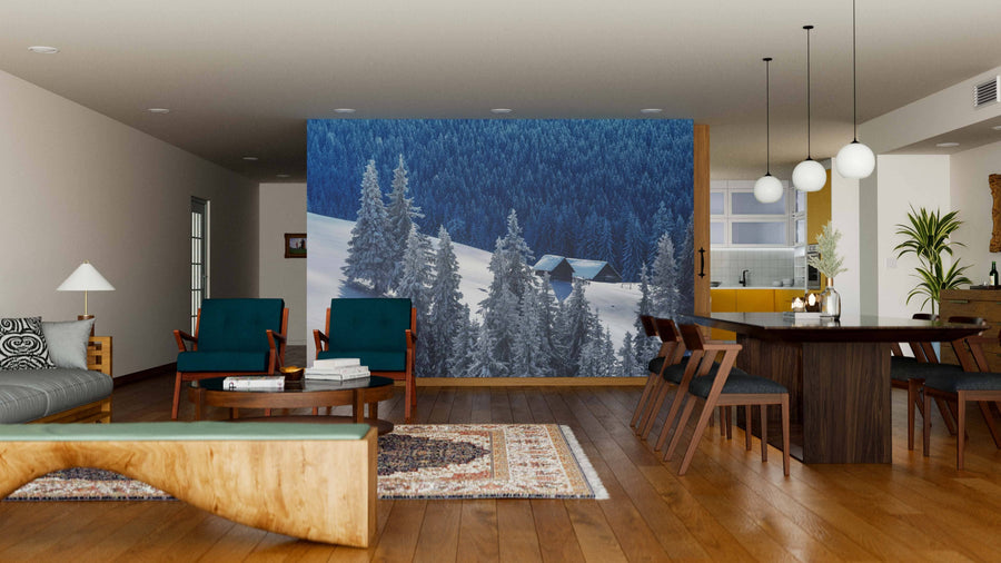 A modern living-dining room features wood floors, dark wood furniture, teal chairs, and the House on the Hill with Snow Wall Mural. Pendant lights, a patterned rug, and a glimpse of the kitchen complete this stylish space.