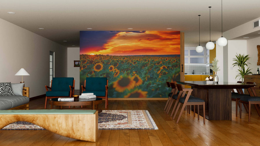 Modern open-concept living and dining area features wood floors, green and wood furniture, and an Illuminated Sunflower Field Wall Mural peel-and-stick at sunset. Pendant lights hang above the table; kitchen is visible in the background.