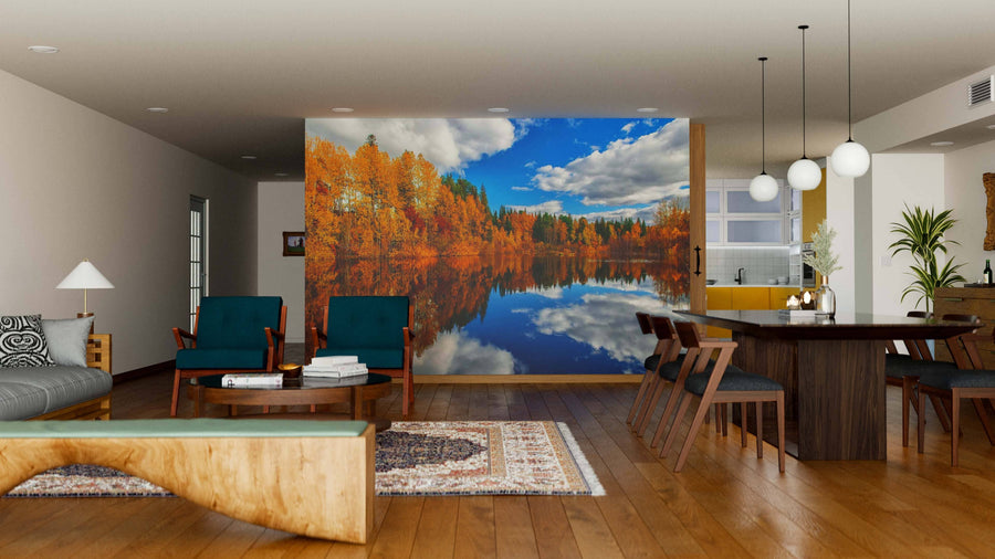 A modern living-dining room with wooden floors and mid-century furniture features the Lake Blue Skies and Fall Colors Wall Mural, creating the illusion of a scenic lake with autumn trees and blue sky indoors.