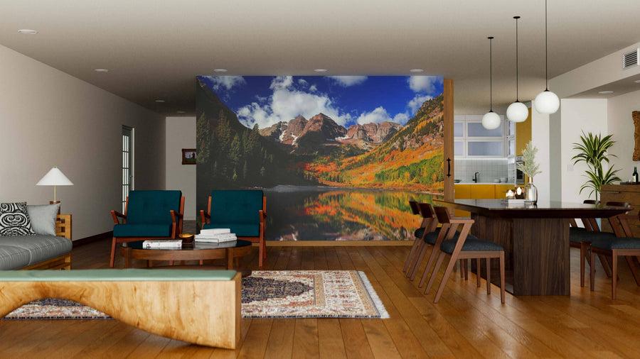 A modern living-dining room with wooden floors and contemporary furniture features the Maroon Bell Mountains Wall Mural, a large peel-and-stick design depicting a scenic mountain lake in autumn, adding depth and rich color to the warm, neutral decor.