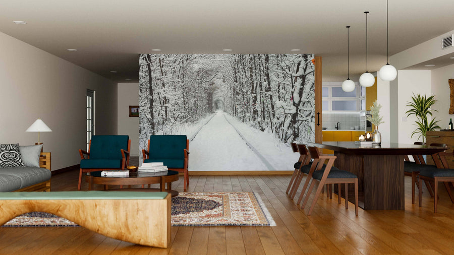 Modern living and dining room with wooden floors and furniture, featuring the 'Railway in the Winter Wall Mural,' a peel and stick mural depicting a snowy forest path lined with leafless trees that adds depth against the warm interior tones.