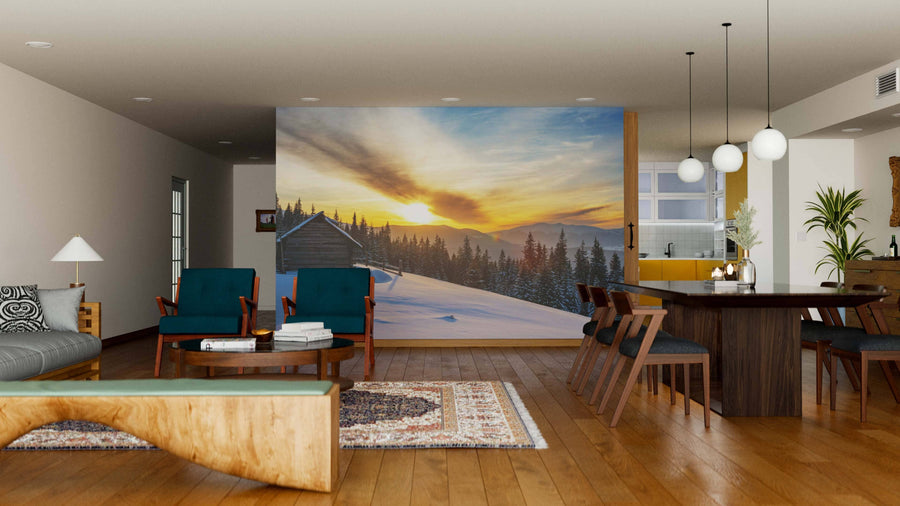A modern living-dining area with wooden floors, teal armchairs, and globe pendants features the "Winter on a Mountain Range Wall Mural," showcasing a snowy landscape with a golden sunset to warm and enliven this cozy, open-concept space.