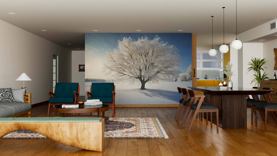 A modern living-dining room with wood floors, blue armchairs, and a gray sofa features the Snow-Covered Tree Wall Mural as a focal point on the far wall, while warm natural light and hanging lamps enhance the contemporary feel.