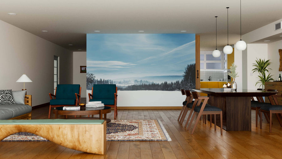 Modern open-plan living and dining room with wood flooring, blue chairs, large table, and globe lights. A wall features the Snowy White Carpathian Mountains Wall Mural, adding a scenic snowy landscape to the cozy, stylish interior.